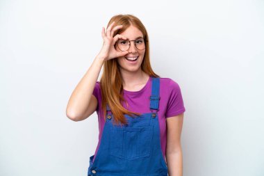 Beyaz arka planda izole edilmiş genç kızıl saçlı kadın parmaklarıyla işaret veriyor.