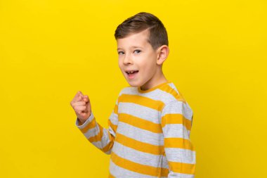 Sarı arka planda izole edilmiş küçük beyaz çocuk zaferi kutluyor.