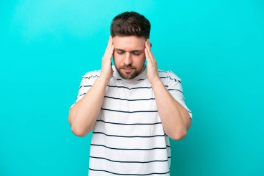 Kafkasyalı genç adam mavi arka planda izole edilmiş, baş ağrısı var.