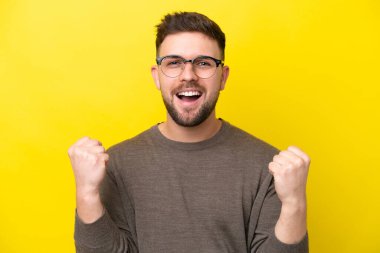Sarı arka planda gözlüklü ve zaferi kutlayan genç beyaz bir adam.