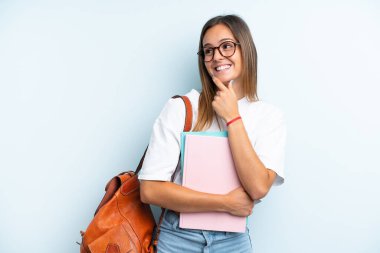 Mavi arka planda izole edilmiş genç bir bayan. Yan tarafa bakıyor ve gülümsüyor.