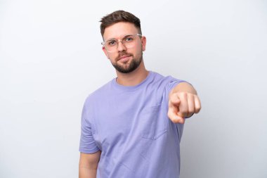 Beyaz arka planda izole edilmiş genç beyaz adam mutlu bir ifadeyle ön tarafı işaret ediyor.