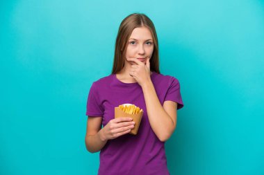 Patates kızartması yakalayan genç Rus kadın mavi arka planda izole edilmiş olarak düşünüyor.