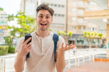 Dışarıda cep telefonu kullanan genç yakışıklı adam şok olmuş bir yüz ifadesiyle.