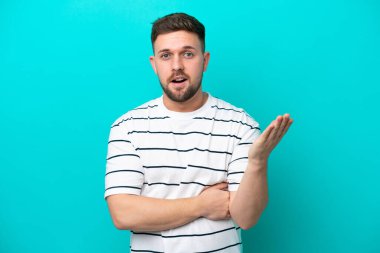 Mavi arka planda izole edilmiş genç beyaz adam şüpheli hareketler yapıyor.