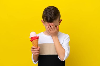 Kornet dondurması olan küçük beyaz çocuk sarı arka planda izole edilmiş yorgun ve hasta bir ifadeyle.
