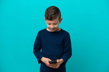 Küçük çocuk mavi arka planda izole edilmiş. Cep telefonuyla mesaj yolluyor.