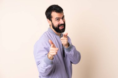 Sakallı, ceketli, soyutlanmış arka planı olan beyaz bir adam şaşırmış ve ön tarafı işaret ediyor.