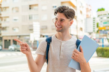 Dışarıdaki yakışıklı öğrenci bir ürün sunmak için yan tarafı işaret ediyor.