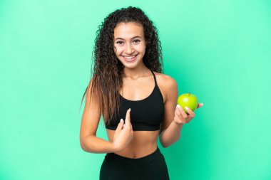 Yeşil arka planda elma izole edilmiş genç bir Arap kadın. Şaşırtıcı bir yüz ifadesi var.