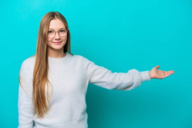 Mavi arka planda izole edilmiş genç bir Rus kadını davet etmek için ellerini yana uzatıyor.