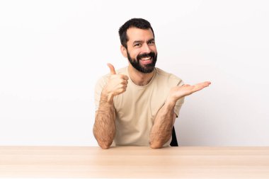 Masada sakallı beyaz bir adam. Avucunun içinde hayali bir şey tutuyor. Bir ilan vermek için..