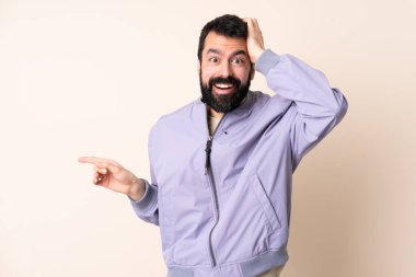 Sakallı, ceketli, soyutlanmış arka planı olan beyaz bir adam şaşırmış ve parmağını kenarı işaret ediyor.