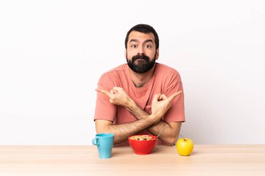 Masada kahvaltı eden beyaz bir adam yan taraftakilerin şüphelerine işaret ediyor..