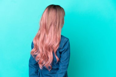 Pembe saçlı melez bir kadın mavi arka planda izole edilmiş ve arkasına bakıyor.