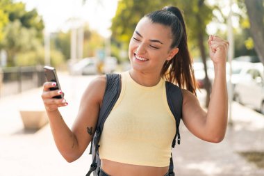 Dışarıda cep telefonu kullanan güzel bir kadın zaferi kutluyor.