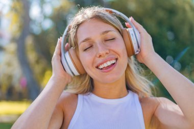 Açık havada müzik dinleyen genç sarışın kadın.