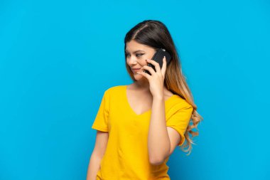 Young girl isolated on blue background keeping a conversation with the mobile phone with someone