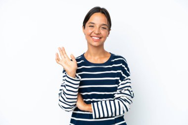 Beyaz arka planda izole edilmiş genç İspanyol kadın mutlu bir ifadeyle selamlıyor.