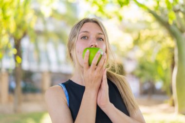 Açık havada, elinde elma tutan genç sarışın kadın.