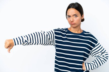 Beyaz arka planda izole edilmiş genç İspanyol kadın, olumsuz bir ifadeyle baş parmağını aşağı gösteriyor.