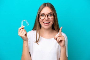 Mavi arka planda izole edilmiş görünmez diş telleri tutan Litvanyalı genç bir kadın harika bir fikre işaret ediyor.
