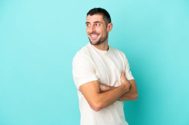 Mavi arka planda izole edilmiş yakışıklı beyaz adam yan tarafa bakıyor ve gülümsüyor.