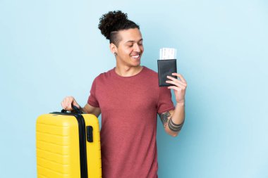 İzole edilmiş mavi geçmişi olan beyaz bir adam, bavul ve pasaportla tatilde.