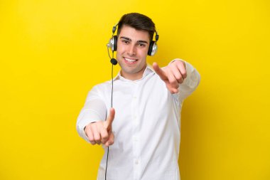 Tele pazarlamacı beyaz bir adam sarı arka planda izole edilmiş bir kulaklıkla çalışıyor.