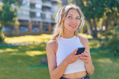 Genç sarışın kadın açık havada müzik dinliyor ve düşünüyor.