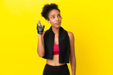 Sarı arka planda izole edilmiş genç Afrikalı kadın parmaklarını çapraz yapıp en iyisini diliyor.