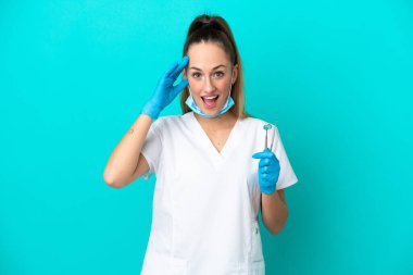 Kafkas dişçi kadın mavi arka planda izole araçlar tutuyor sürpriz bir ifadeyle