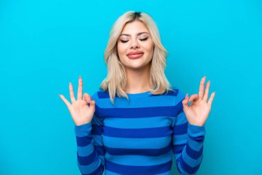 Zen pozisyonunda mavi arka planda izole edilmiş genç bir kadın.