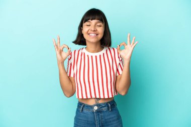 Genç melez kadın, mavi arka planda Zen pozisyonunda izole edilmiş.