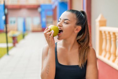 Dışarıda elma yiyen genç ve güzel bir kadın.