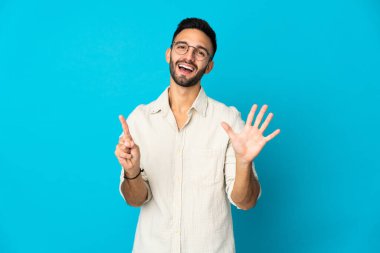 Mavi arka planda izole edilmiş genç beyaz adam parmaklarıyla altısını sayıyor.