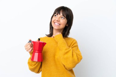 Beyaz arka planda kahve demliği tutan genç bir ırk kadını gülümserken yukarı bakıyor.