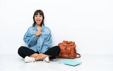 Beyaz arka planda izole bir katta oturan genç bayan şaşırmış ve işaret ediyor.