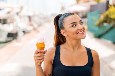 Açık havada kornet dondurmalı güzel bir kadın gülümserken yukarı bakıyor.