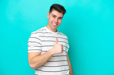 Kafkasyalı genç adam mavi arka planda izole edilmiş bir şekilde baş parmak işareti yapıyor.