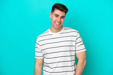 Kafkasyalı genç adam mavi arka planda tek başına gülüyor.