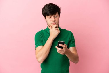 Genç Rus bir adam pembe arka planda izole edilmiş düşünüyor ve bir mesaj gönderiyor.
