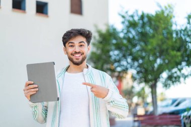 Yakışıklı bir Arap, elinde tablet tutarken yüzünde şaşkınlık ifadesi var.