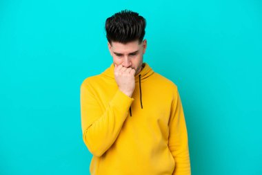 Kafkasyalı genç adam mavi arka planda izole edilmiş. Şüpheleri var.