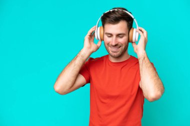 Genç beyaz adam mavi arka planda izole edilmiş müzik dinliyor.