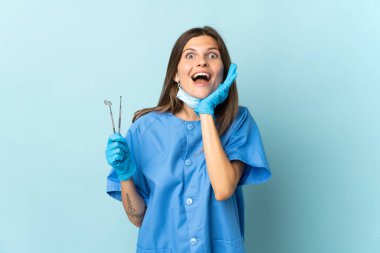 Slovak dişçi mavi arka planda izole araçlar tutuyor sürpriz ve şok yüz ifadesi ile