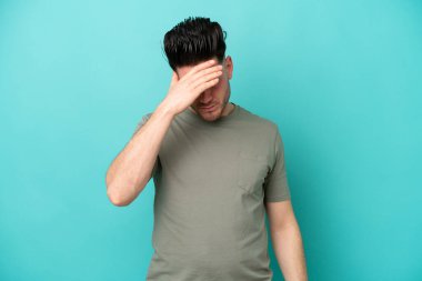 Kafkasyalı genç adam mavi arka planda izole edilmiş, baş ağrısı var.