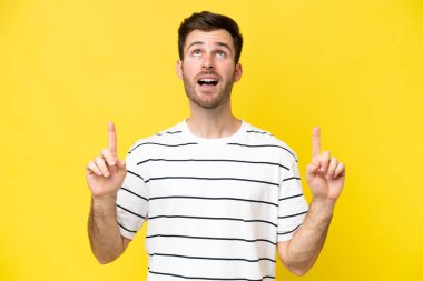 Sarı arka planda izole edilmiş genç beyaz adam şaşırmış ve yukarı bakıyor.