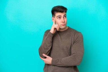 Kafkasyalı genç adam mavi arka planda izole edilmiş. Şüpheleri ve düşünceleri var.
