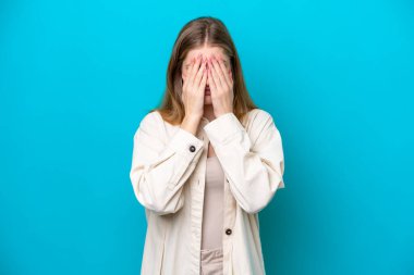 Genç Rus kız mavi arka planda izole edilmiş, gözleri elle kapatılmış.
